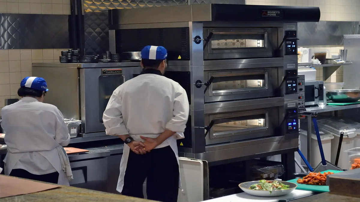 Deux chefs de cuisine devant des fours professionnels dans un restaurant, un secteur où la gestion de la fiche Google demande une approche spécifique